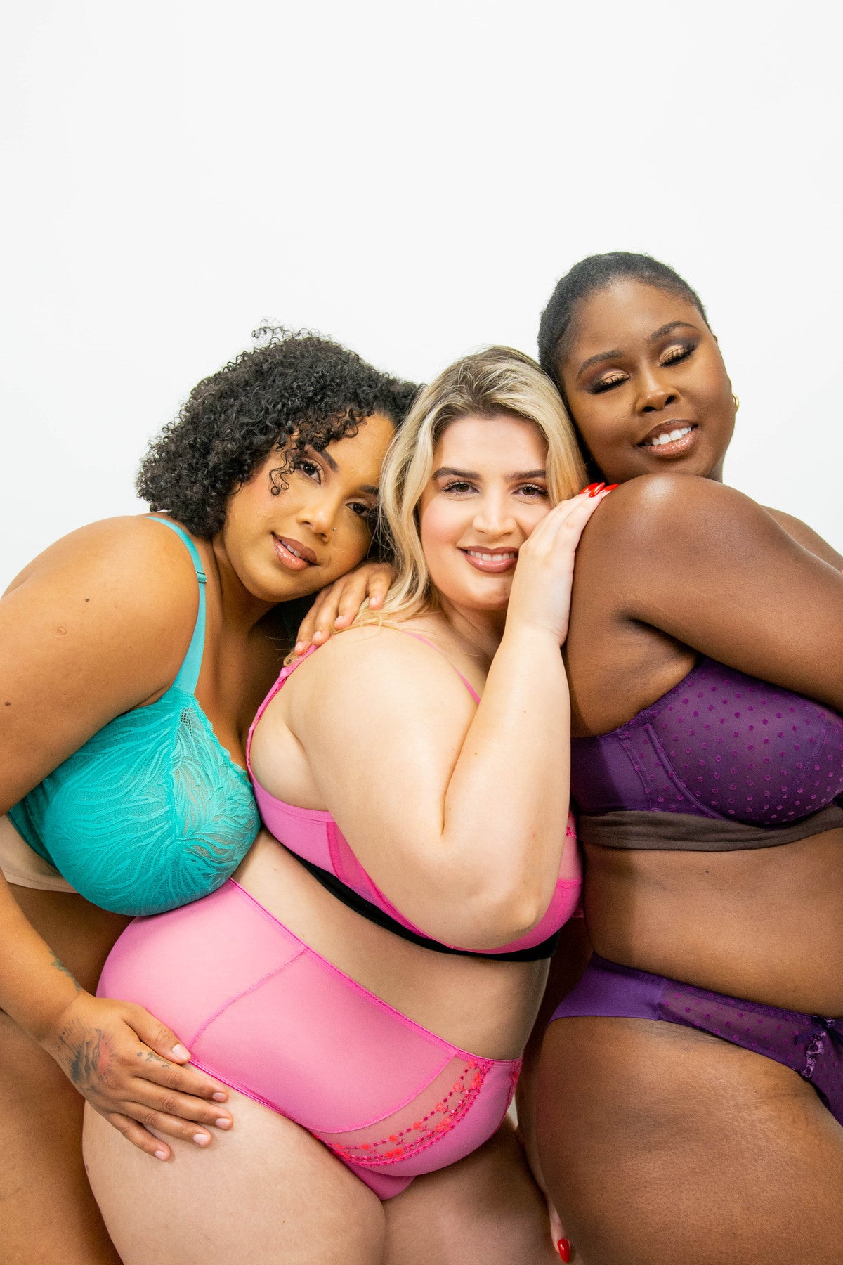 Three large chested models pose together while wearing bra liners under their bras.