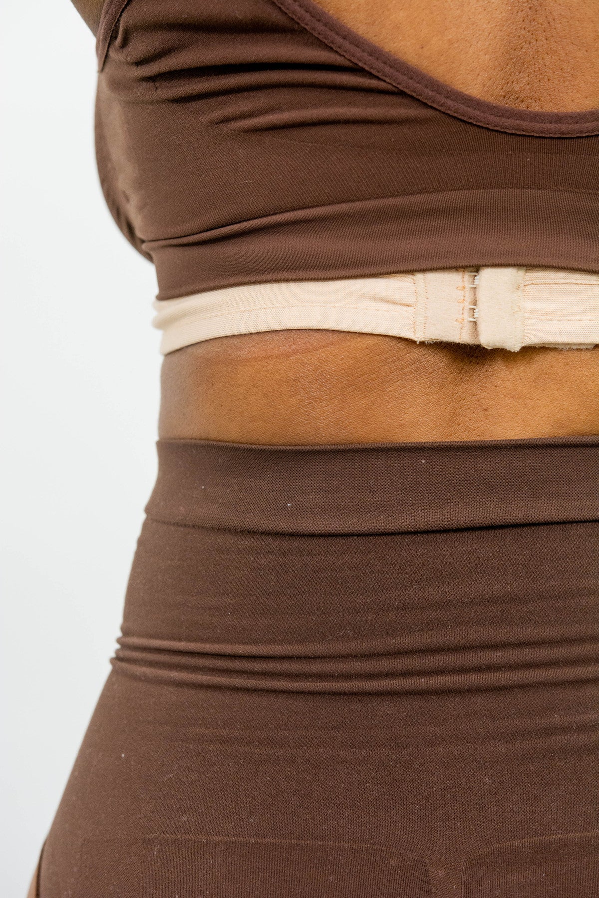 A beige body pH bra liner is fastened at the back under a brown bra using hooks and colsures.