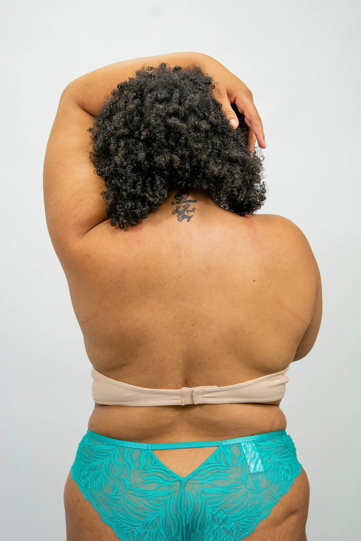 A braless model with black hair wears the bra liner as seen from the back. The liner is fastened with hook and eye closures and secured in place.