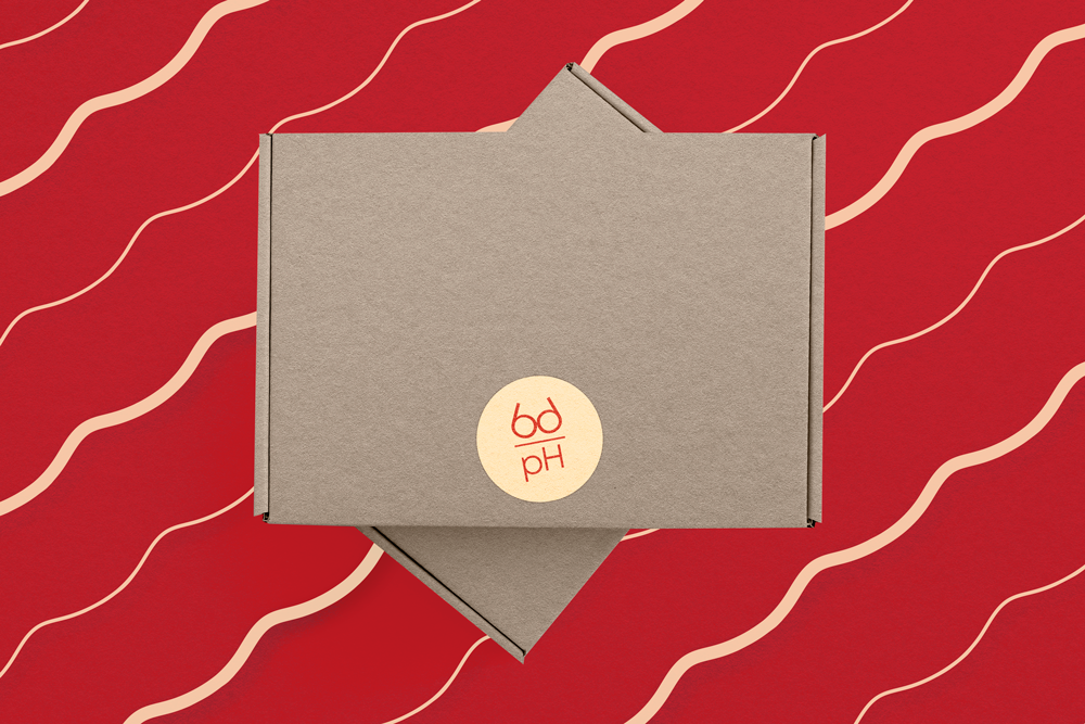 An image of the body pH packaging, which shows red and beige patterned tissue paper in the background, recycled cardboard boxes, and a beige logo sticker on the boxes.